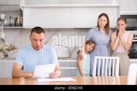 Un père mécontent lit attentivement les documents. Toute la famille est dans la peur en arrière-plan Banque D'Images