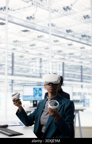 Femme afro-américaine portant un casque VR dans le bureau RD d'usine de micropuce pour regarder les dispositions de circuit immersives. Ingénieur féminin utilisant la réalité virtuelle pour créer des conceptions de matériel PCB dans le centre de recherche Banque D'Images