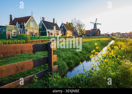 Village de campagne hollandais traditionnel avec des maisons en bois historiques, canal et moulin à vent dans la lumière chaude de l'heure dorée du soleil, montrant la vie rurale paisible et au Banque D'Images