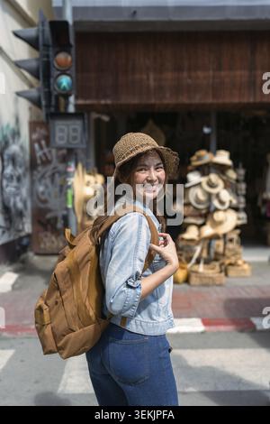 Jeune femme touriste marchant de l'autre côté de la rue et regardant la caméra tout en voyageant dans le marché local Banque D'Images