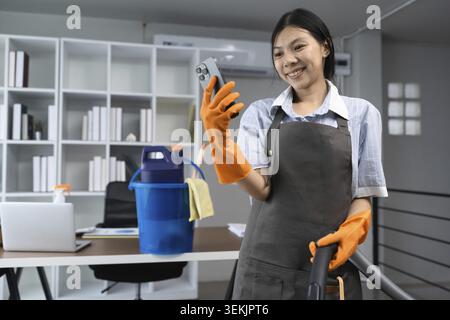 Application pour les travaux ménagers sur smartphone. Jeune femme de ménage tenant le téléphone portable pour appeler le service Housekeep nettoyage maison Banque D'Images