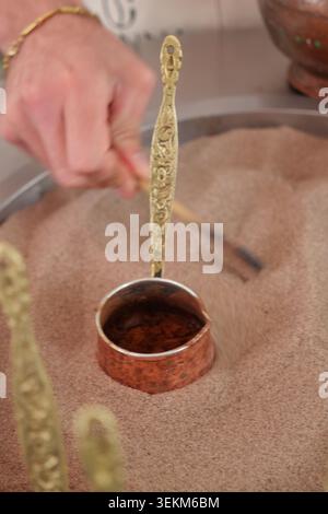 Main à l'aide d'une cuillère pour préparer le café turc dans la chaleur du sable Banque D'Images