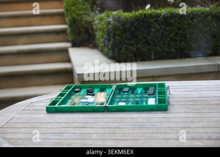 Plateau de backgammon vert installé sur une table de jardin en bois pour un jeu en plein air dans un cadre de patio privé. Banque D'Images