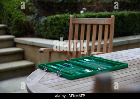Plateau de backgammon vert installé sur une table de jardin en bois pour un jeu en plein air dans un cadre de patio privé. Banque D'Images