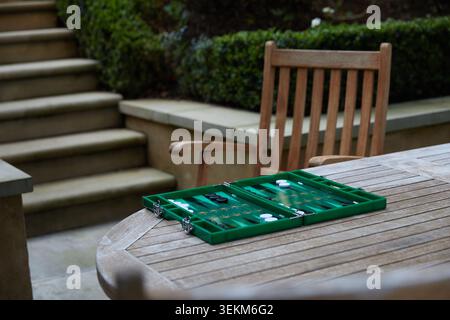 Plateau de backgammon vert installé sur une table de jardin en bois pour un jeu en plein air dans un cadre de patio privé. Banque D'Images