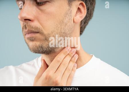 L'homme malsain tient le cou ressent des douleurs aiguës à la gorge, une inflammation due au reflux acide, des ganglions lymphatiques gonflés dus à la maladie. Infections virales ou bactériennes, tonsi Banque D'Images