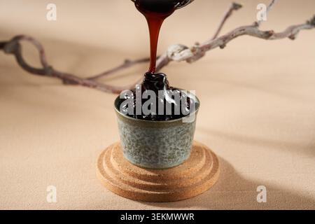 Le sirop noir brun foncé est lentement versé sur les perles dans la tasse en céramique, coulant soyeusement et donnant une texture chaude Banque D'Images