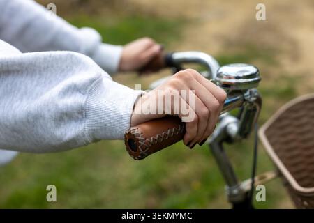 Mains d'enfant tenant le guidon de vélo vintage. Gros plan de mains d'enfant saisissant un guidon de vélo en cuir marron avec cloche chromée lors d'un extérieur Banque D'Images