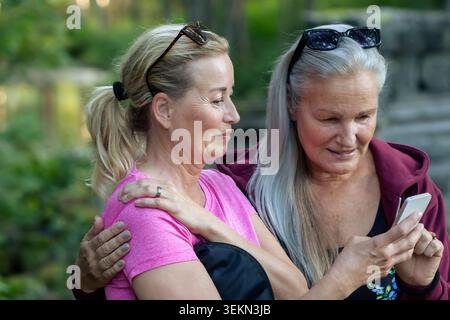 Femme senior souriante partageant un téléphone intelligent avec une amie au parc Banque D'Images