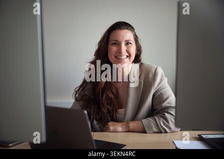 Portrait d'entrepreneur féminin aux cheveux longs souriants assis au bureau Banque D'Images