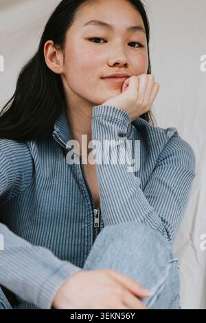 Portrait d'une jeune femme assise tout en s'appuyant sur le coude contre toile de fond Banque D'Images
