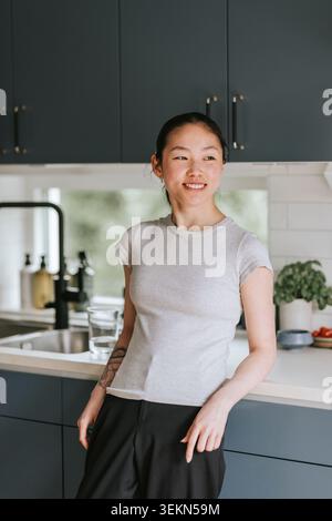 Jeune femme souriante appuyée sur le comptoir de cuisine à la maison Banque D'Images