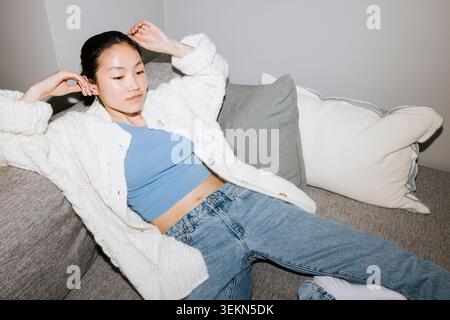 Vue en angle élevé d'une jeune femme portant une veste couchée sur un canapé à la maison Banque D'Images
