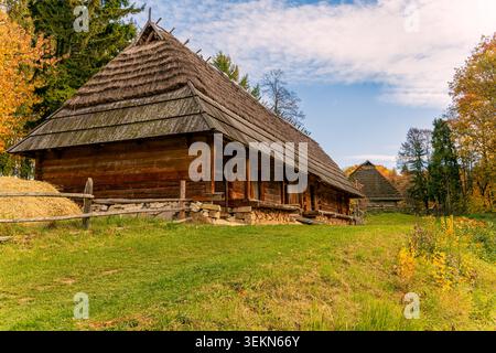 Scène de village rural traditionnel avec de vieilles cabanes en bois nichées au milieu du feuillage d'automne animé sous un ciel bleu vif Banque D'Images