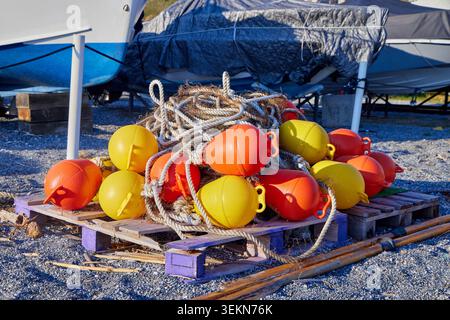 Bouées marines jaune vif et orange avec des cordes empilées sur des palettes en bois dans une cour de bateaux. Banque D'Images