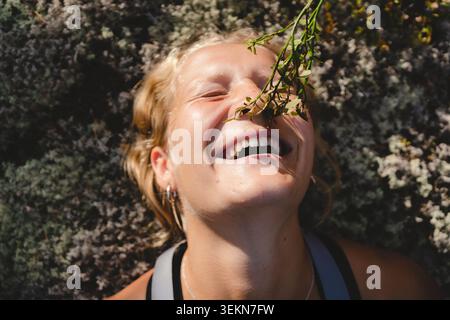 Vue rapprochée de la femme heureuse avec les yeux fermés couchés sur des fleurs au jour ensoleillé Banque D'Images