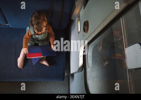 Directement au-dessus de la vue du bébé garçon jouant avec le livre tout en étant assis sur le siège dans le train Banque D'Images