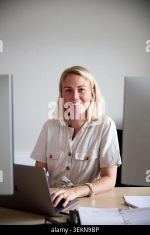 Portrait d'une femme professionnelle souriante assise avec un ordinateur portable sur le bureau dans le bureau Banque D'Images