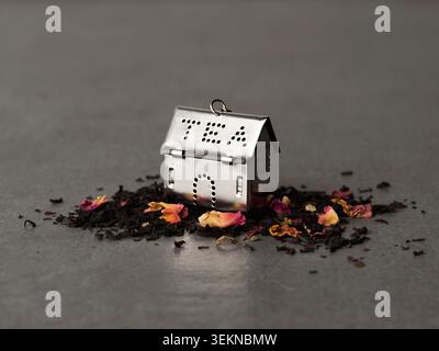 Plan d'infuseur de thé argenté en forme de maison sur pile de thé en feuilles en vrac Banque D'Images