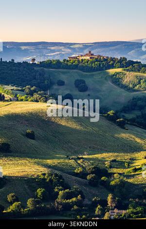 Montefabbri village perché sur sa colline à Montefeltro, Italie, illuminé par la lumière douce du lever du soleil sur les collines verdoyantes. Banque D'Images