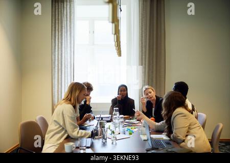 Groupe de professionnels d'entreprise divers communiquant tout en étant assis autour d'une table dans la salle de réunion Banque D'Images