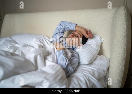 Malheureuse femme aînée réfléchie couchée au lit le matin à la maison avec une expression épuisée perdue, femme âgée dans la chambre montrant la solitude et la dépression à un âge plus avancé, crise de la vie et des problèmes mentaux. Banque D'Images