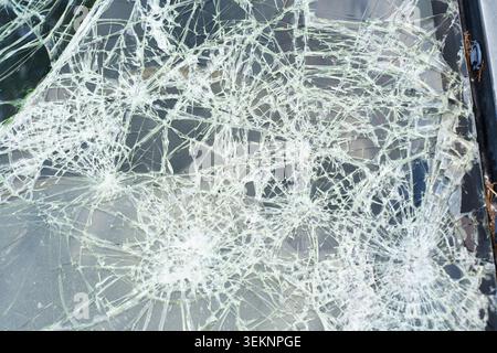 Gros plan du pare-brise brisé de voiture affichant plusieurs points d'impact et des motifs complexes de fissures en toile d'araignée. Verre de sécurité feuilleté endommagé par lourd Banque D'Images