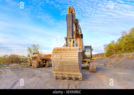 Gros plan d'un grand godet jaune posé sur le sol avec un tombereau articulé garé à l'arrière-plan sur une construction extérieure s Banque D'Images