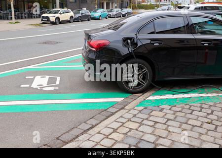 Une voiture hybride Mercedes-Benz classe A noire se chargeant à une station EV dans une rue de ville européenne, vue arrière en gros plan. Banque D'Images