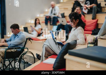 Divers étudiants étudiant dans un espace de conférence moderne à plusieurs niveaux, y compris un étudiant en fauteuil roulant Banque D'Images