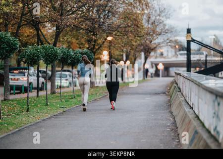 Deux femmes faisant du jogging ensemble le long d'un chemin de parc urbain en soirée d'automne pour la remise en forme et l'amitié Banque D'Images