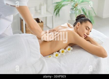 Femme souriante allongée sur la table de massage avec les yeux fermés, profitant d'un massage relaxant du dos dans le salon de spa. Banque D'Images