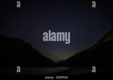 Étoiles remplissant le ciel nocturne sombre au-dessus des sommets de montagne et rivière calme avec des aurores légères Banque D'Images