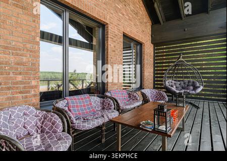 Espace extérieur accueillant avec un mur de briques, des sièges confortables, une table en bois et une chaise suspendue élégante, créant une atmosphère relaxante et confortable Banque D'Images
