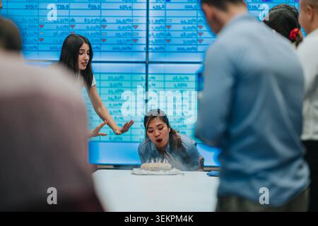 Les collègues d'affaires célèbrent un anniversaire dans un bureau avec un gâteau et des écrans numériques en arrière-plan Banque D'Images