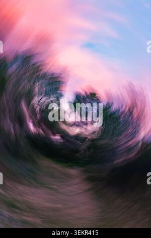 Une photographie abstraite artistique mettant en vedette une technique de rotation intentionnelle de la caméra qui crée un effet de flou de mouvement tourbillonnant sur les arbres verts sous un V. Banque D'Images