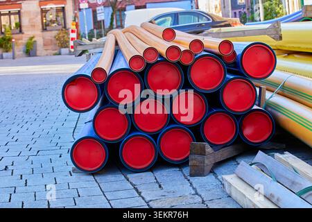 Tuyaux de service publics en plastique bleu et marron avec embouts de protection rouges empilés sur une rue pavée sur un chantier municipal de construction. Banque D'Images