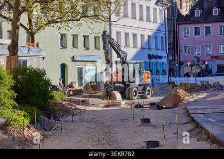 Excavatrice sur roues travaillant sur un chantier de rénovation de rue et de construction de route devant des bâtiments historiques par une journée ensoleillée en Allemagne. Banque D'Images