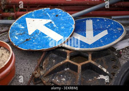Panneaux de signalisation bleus rayés avec des flèches blanches jetés sur la pile de ferraille. Banque D'Images