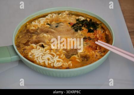 Nouilles ramen épicées cuisant dans une poêle verte sur une cuisinière à induction Banque D'Images
