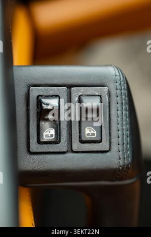 Gros plan des deux commutateurs de lève-glaces électriques noirs avec emblèmes blancs emblématiques, dans un accoudoir sophistiqué garni de cuir noir d'un luxe Banque D'Images