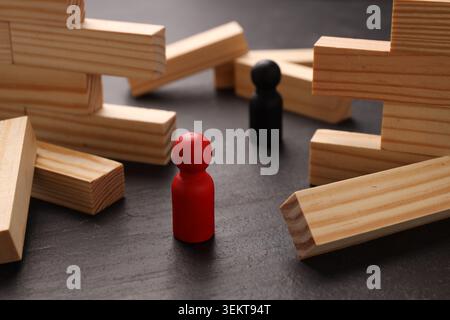 Mur en bois effondré fait de blocs et de figures humaines sur la table noire, gros plan. Surmonter les obstacles Banque D'Images