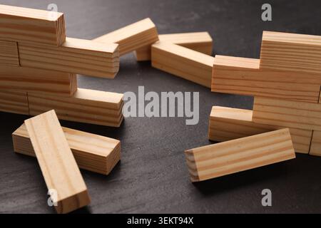 Mur en bois effondré fait de blocs sur la table noire, gros plan. Surmonter les obstacles Banque D'Images