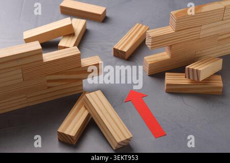 Mur en bois effondré fait de blocs et flèche de papier sur la table grise, gros plan. Surmonter les obstacles Banque D'Images