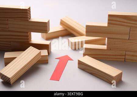 Mur en bois effondré fait de blocs et flèche de papier rouge sur fond blanc, gros plan. Surmonter les obstacles Banque D'Images