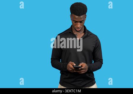 Homme afro-américain interagissant avec un téléphone portable sur fond bleu Banque D'Images