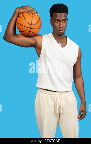Jeune homme africain tenant un basket-ball regardant déterminé sur un fond bleu Banque D'Images