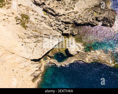 Vue aérienne du trou bleu à Dwejra Bay avec des gens nageant dans la piscine naturelle entourée de falaises de calcaire escarpées dans la région de Gozo, Malte. Banque D'Images