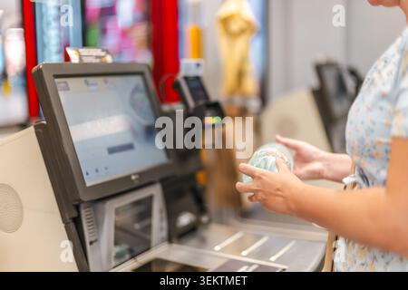 Femme utilisant le kiosque de caisse libre-service dans le supermarché, scannant le produit d'épicerie et complétant l'achat par le système automatisé de paiement au détail Banque D'Images