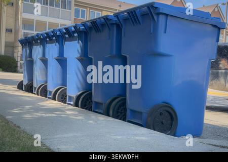 Rangée de bacs de recyclage bleus placés le long d'une rue résidentielle en attente de collecte. Concept de service de gestion et de recyclage des déchets municipaux en banlieue Banque D'Images